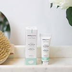 Green People Organic Firming Eye Serum next to the cardboard box packaging on a marble surface in a bathroom setting. 
