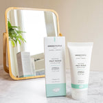 Green People Fruit Scrub Exfoliator tube pictured next to the cardboard packaging in front of a gold rimmed mirror. 