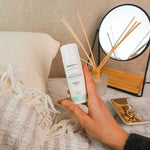 A person holding a bottle of Green People Fruitful Nights Night Cream in their hand. The cream is being held above a dressing table. 
