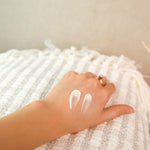 A swatch of the Green People Fruitful Nights Night Cream on a hand. The person is resting their hand on a striped blanket. 