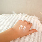 A swatch of the Green People Fruitful Nights Night Cream on a hand. The person is resting their hand on a striped blanket. 
