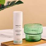 Green People Hydrating Firming Serum placed on a rectangular bamboo dish next to a green glass tealight holder. 