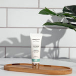 A tube of Green People Rejuvenating Eye Cream placed on an oval shaped bamboo tray in a bathroom. 