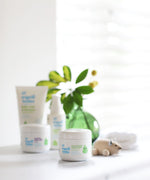 Organic Babies mum & baby Scent Free rescue balm placed on a white surface next to a wooden toy mouse. Other products from the organic babies collection can be seen in the background. 