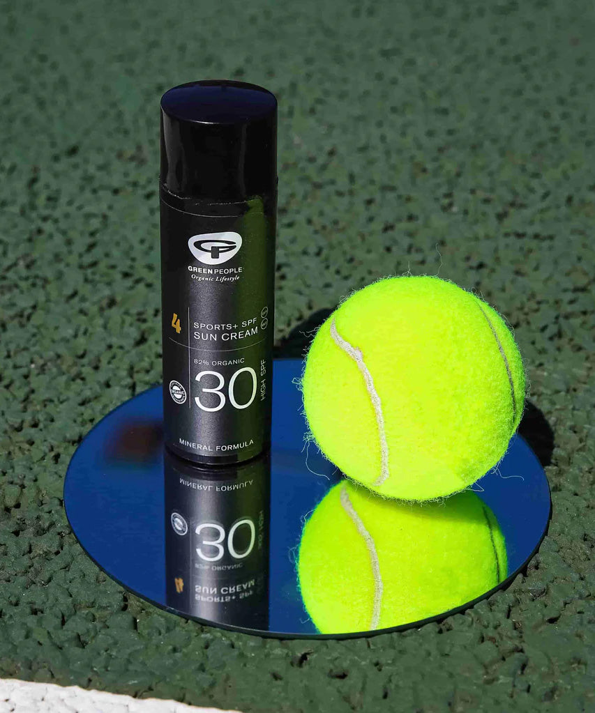 The Green People Sports+ Sun Cream in black sun resistant packaging, next to a tennis ball.