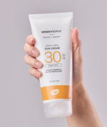 A tube of Green People Sun Cream SPF30 in an adult's hand. 