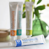 Tube of Organic People peppermint and aloe vera toothpaste laid flat next to other toothpastes 