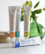 Tube of Organic People peppermint and aloe vera toothpaste laid flat next to other toothpastes 