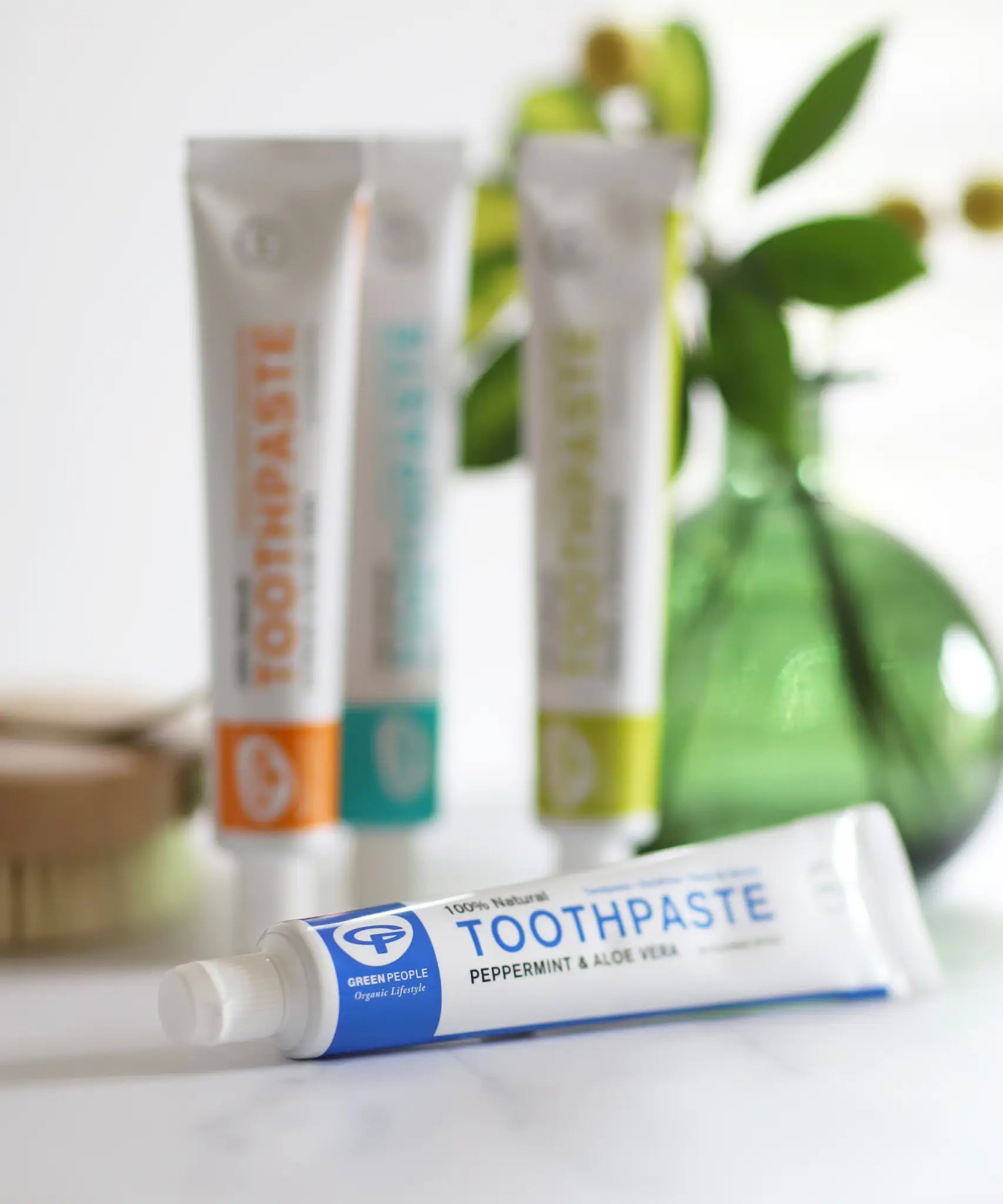 Tube of Organic People peppermint and aloe vera toothpaste laid flat next to other toothpastes 