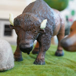 Green rubber toys sustainable rubber bison stood on some green felt behind a small papoose rock toy