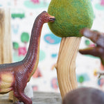 Close up of a green rubber toys sustainable dinosaur next to a papoose wooden tree toy