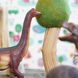 Close up of a green rubber toys sustainable dinosaur next to a papoose wooden tree toy