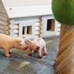 Close up of the green rubber toys pig and piglet figures on some grey felt in front of a small wooden hut toy