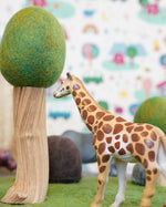 Close up of a green rubber toys giraffe figure on some green felt next to a papoose wooden tree toy