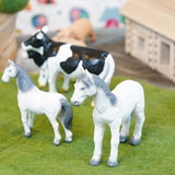 Green rubber toys horses stood on some green felt in front of some green rubber toys cows