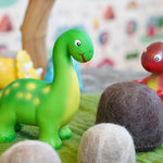 Close up of the green rubber toys eco-friendly mini dinosaurs stood on some green felt behind a papoose felt rock toy