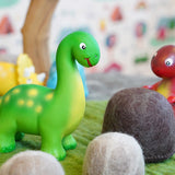 Close up of the green rubber toys eco-friendly mini dinosaurs stood on some green felt behind a papoose felt rock toy