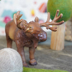 Close up of a green rubber toys moose figure on some grey felt in front of a papoose wooden tree toy