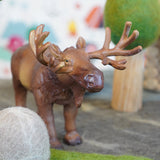 Close up of a green rubber toys sustainable moose figure on some grey felt in front of a papoose wooden tree