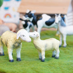 Green rubber toys sustainable sheep figures stood on some green felt in front of a horse and cow toy