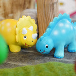 Close up of the green rubber toys mini dinosaurs stood on some grey felt in front of a papoose tree toy