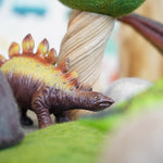 Close up of a green rubber toys stegosaurus toy on some green felt hidden behind a papoose rock toy