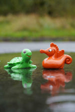 green turtle and orange red seahorse from the Green Rubber Toys Sea Friends Bath Toy Set pictured in a puddle of water outdoors