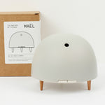 Maël Diffuser, a light grey dome plug-in essential oil diffuser with wooden feet, and cardoard packaging behind. 