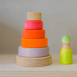 Grimm's Small Conical Stacking Tower - Neon Pink - On a plain blue background. Grimm's Neon Pink Friends are in front and behind the Tower.