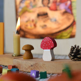 A Grimm's fly agaric red and white mushroom decorative figure placed on a natural celebration ring. A Toverlux lamp can be seen in the background.