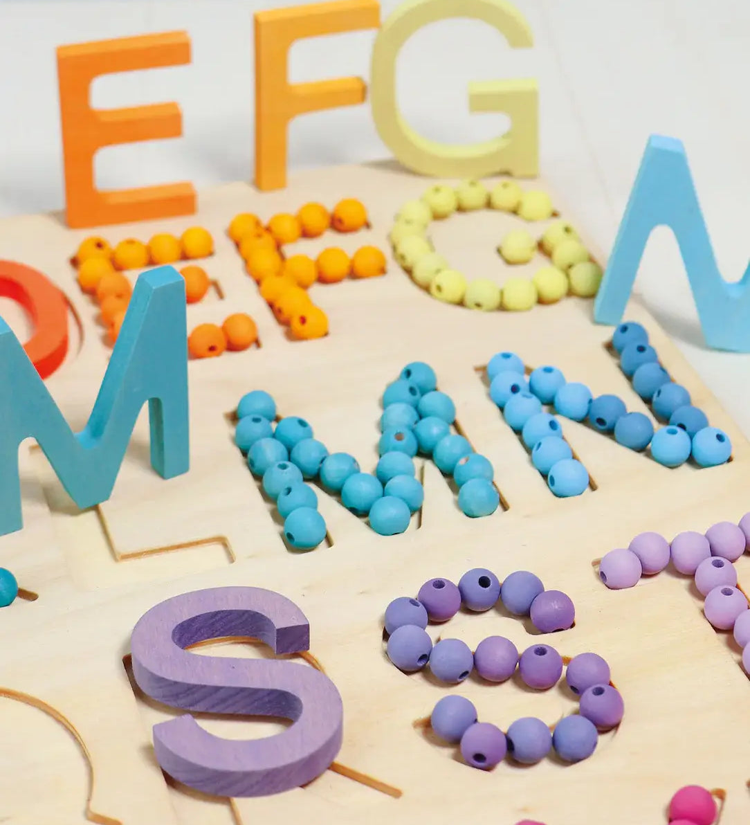 Grimms wooden alphabet board with 12mm beads in a pastel palette filling  the letter cut outs