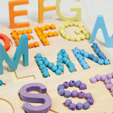 Grimms wooden alphabet board with 12mm beads in a pastel palette filling  the letter cut outs
