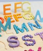 Grimms wooden alphabet board with 12mm beads in a pastel palette filling  the letter cut outs