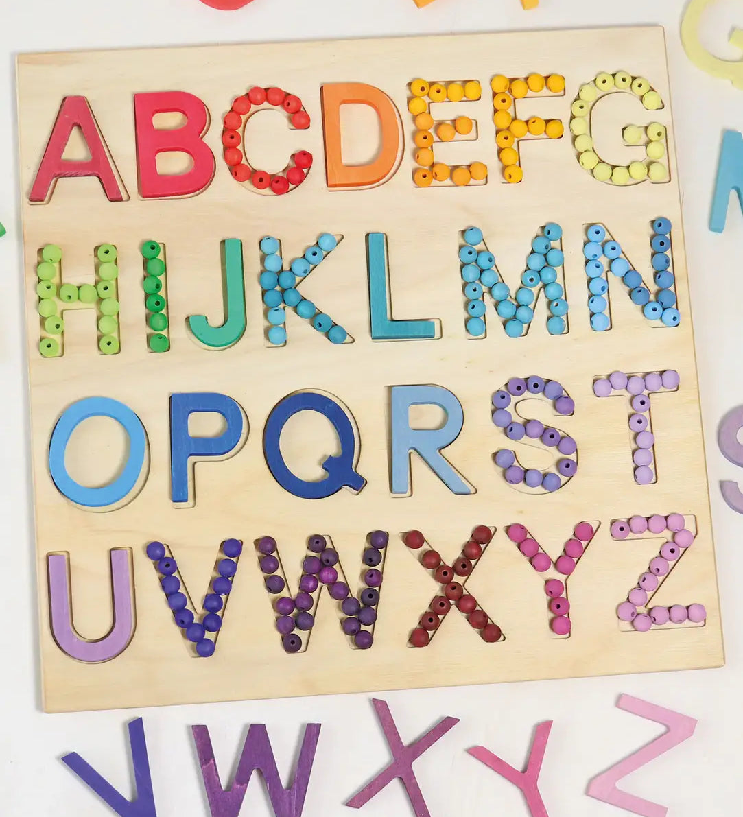 Grimms wooden alphabet board with the rainbow and pastel 12mm beads filling in the letter cut outs