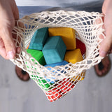 Adults holding the Grimm's 15 rainbow coloured wooden toy building blocks in the net storage bag.