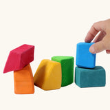 Adult's hand holding a blue block from the Grimm's 15 rainbow coloured wooden toy building blocks.