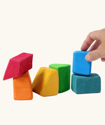 Adult's hand holding a blue block from the Grimm's 15 rainbow coloured wooden toy building blocks.