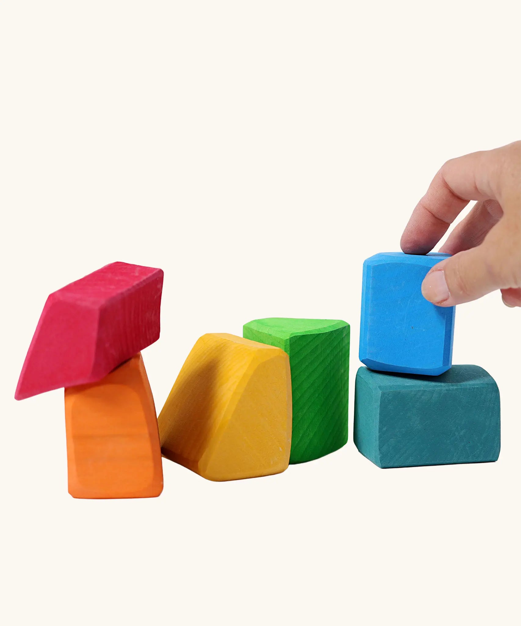 Adult's hand holding a blue block from the Grimm's 15 rainbow coloured wooden toy building blocks.