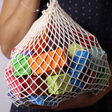 Adult holding the Grimm's 15 rainbow coloured wooden toy building blocks in a net storage bag.