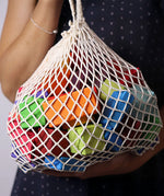 Adult holding the Grimm's 15 rainbow coloured wooden toy building blocks in a net storage bag.