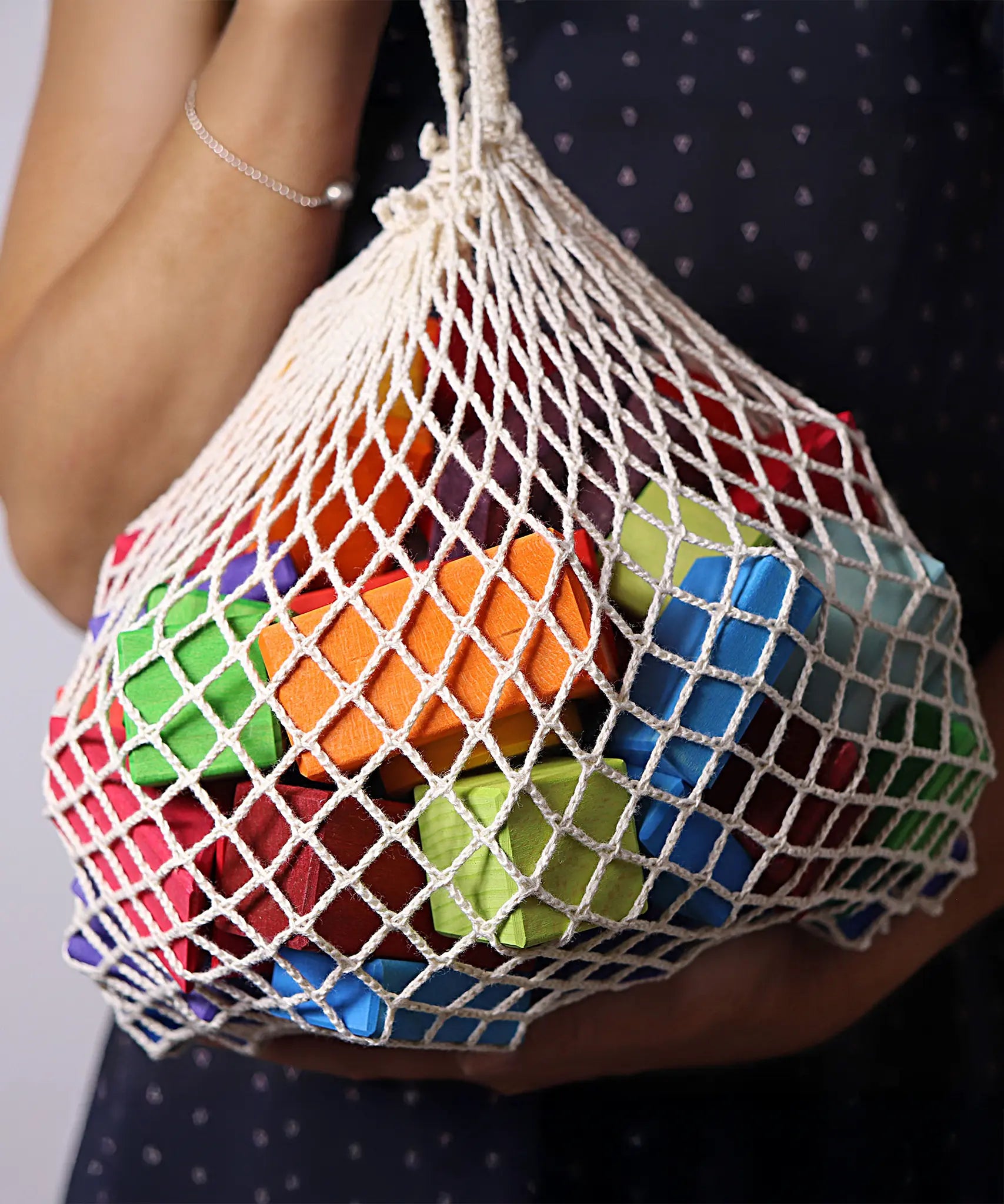 Adult holding the Grimm's 15 rainbow coloured wooden toy building blocks in a net storage bag.