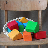 Grimm's 15 rainbow coloured wooden toy building blocks in a net storage bag on a wooden chair.