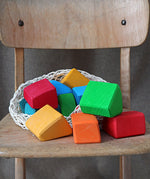 Grimm's 15 rainbow coloured wooden toy building blocks in a net storage bag on a wooden chair.