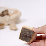 Grimm's 15 wooden blocks with natural bark, one block shown in an adult's hand.