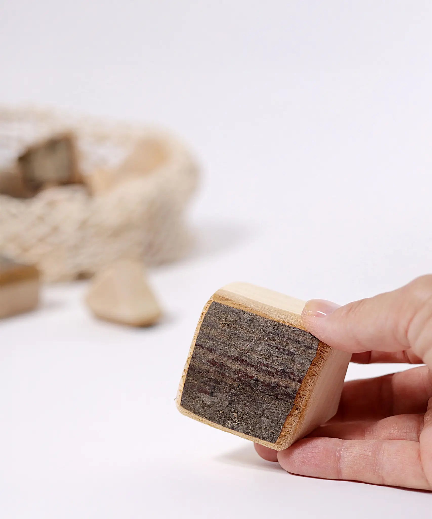 Grimm's 15 wooden blocks with natural bark, one block shown in an adult's hand.