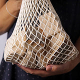 Grimm's 15 wooden blocks with natural bark in a net storage bag held in an adult's hands.