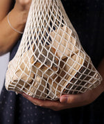 Grimm's 15 wooden blocks with natural bark in a net storage bag held in an adult's hands.