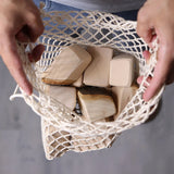 Grimm's 15 wooden blocks with natural bark in a net storage bag held in an adult's hands.