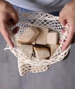 Grimm's 15 wooden blocks with natural bark in a net storage bag held in an adult's hands.