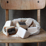 Grimm's 15 wooden blocks with natural bark in a net storage bag placed on a wooden chair.
